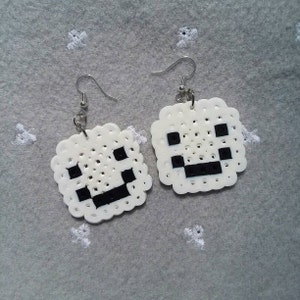 May include: A pair of white and black pixelated smiley face earrings. The earrings are made of white beads with black beads forming the eyes and mouth.