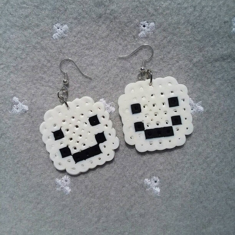 May include: A pair of white and black pixelated smiley face earrings. The earrings are made of white beads with black beads forming the eyes and mouth.