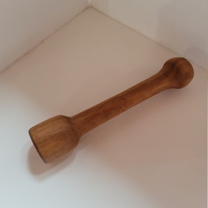 May include: A wooden kitchen tool with a rounded end and a slightly thicker handle. The tool is made of light brown wood and is about 25 cm long.