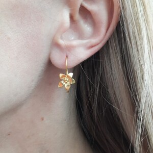 Peut inclure: Boucles d'oreilles pendantes en forme de fleur dor&eacute;es. Les boucles d'oreilles sont petites et d&eacute;licates, avec un design simple. La fleur est un design &agrave; cinq p&eacute;tales avec un petit centre.