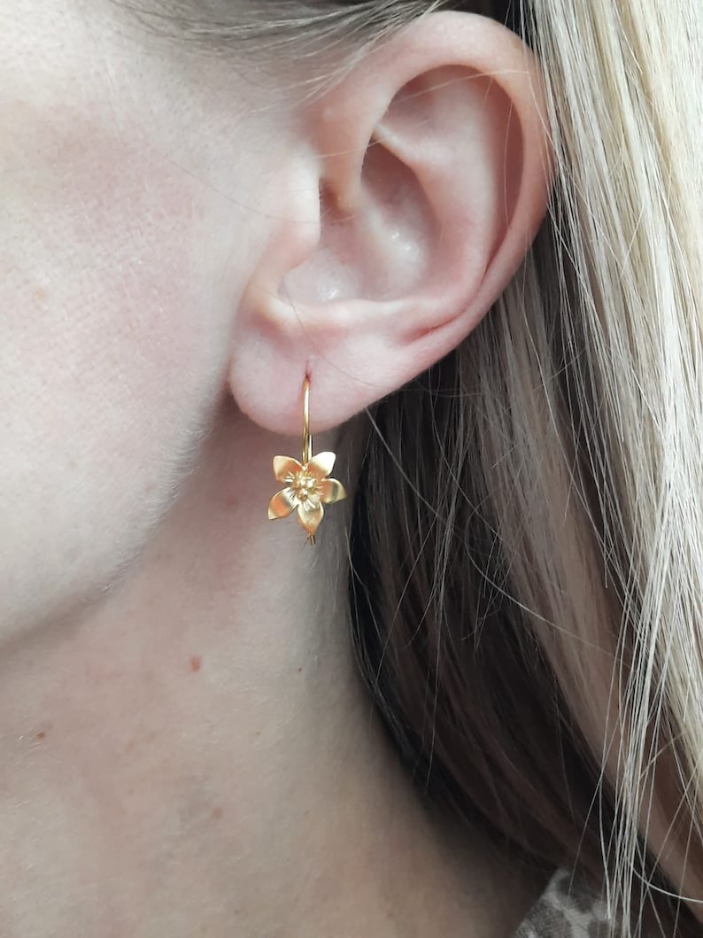Peut inclure: Boucles d'oreilles pendantes en forme de fleur dor&eacute;es. Les boucles d'oreilles sont petites et d&eacute;licates, avec un design simple. La fleur est un design &agrave; cinq p&eacute;tales avec un petit centre.