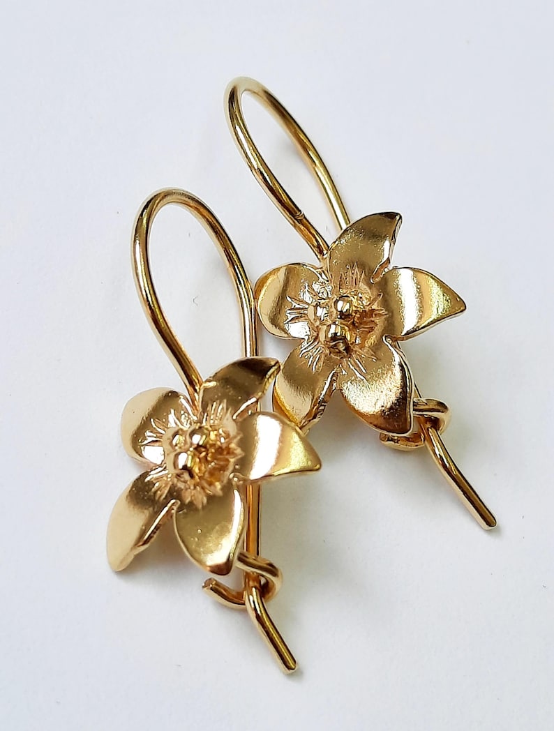 Peut inclure: Une paire de boucles d'oreilles en forme de fleur dor&eacute;es avec un design d&eacute;licat. Les boucles d'oreilles ont une fermeture simple &agrave; crochet.