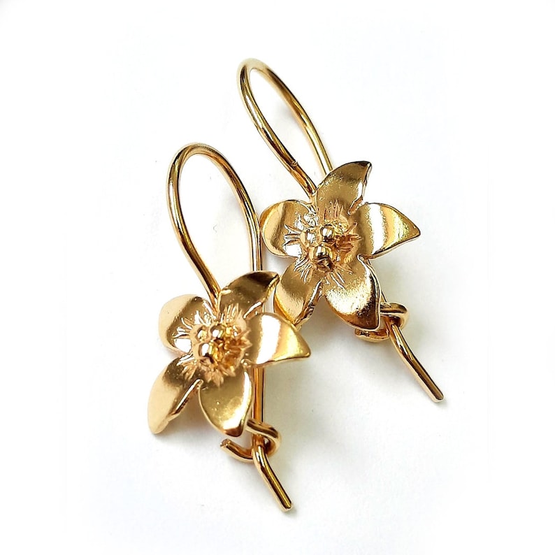 Peut inclure: Une paire de boucles d'oreilles pendantes en forme de fleur dor&eacute;es avec un design d&eacute;licat. Les boucles d'oreilles sont en m&eacute;tal dor&eacute; et ont un motif floral.