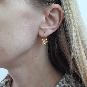 Peut inclure: Boucles d'oreilles en forme de fleur dor&eacute;es avec un design d&eacute;licat. Les boucles d'oreilles pendent &agrave; l'oreille d'une personne.