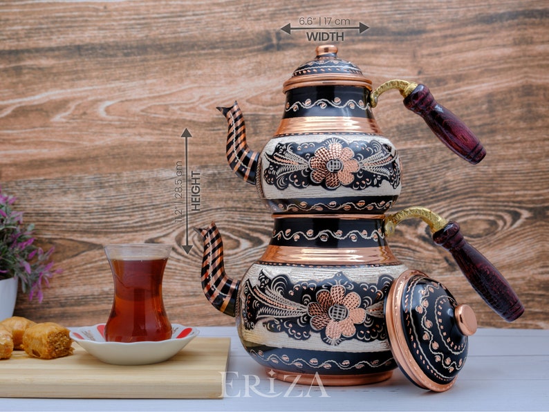 Puede incluir: Una tetera de cobre de dos niveles con dise&ntilde;os florales en blanco y negro y detalles en cobre. La tetera tiene dos asas de madera y una tapa. La tetera mide 31,1 cm de alto y 16,8 cm de ancho.