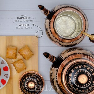 Puede incluir: Dos teteras de cobre con dise&ntilde;os negros y cobre, una con mango de madera y una taza peque&ntilde;a de cobre. Las teteras est&aacute;n sobre una superficie blanca. Hay una tabla de cortar de madera con tres trozos de baklava encima. Tambi&eacute;n hay un peque&ntilde;o platillo blanco con un dise&ntilde;o rojo y blanco y un vaso de t&eacute; encima. El texto de la imagen dice "CAPACIDAD TOTAL 96.3 oz | 2850 ml PESO 35.9 oz | 1020 g"