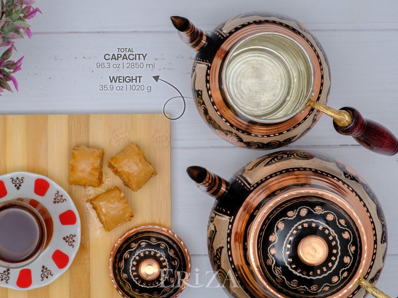 Puede incluir: Dos teteras de cobre con dise&ntilde;os negros y cobre, una con mango de madera y una taza peque&ntilde;a de cobre. Las teteras est&aacute;n sobre una superficie blanca. Hay una tabla de cortar de madera con tres trozos de baklava encima. Tambi&eacute;n hay un peque&ntilde;o platillo blanco con un dise&ntilde;o rojo y blanco y un vaso de t&eacute; encima. El texto de la imagen dice "CAPACIDAD TOTAL 96.3 oz | 2850 ml PESO 35.9 oz | 1020 g"