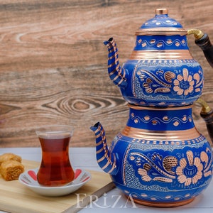 Puede incluir: Un juego de t&eacute; turco azul y cobre con intrincados dise&ntilde;os florales. El juego incluye una tetera con asa de madera y un vaso de t&eacute;.