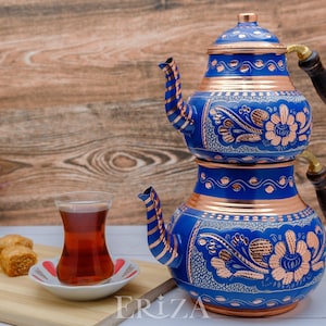 May include: A blue and copper Turkish tea set with intricate floral designs. The set includes a teapot with a wooden handle and a glass of tea.