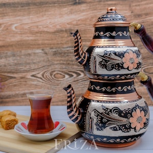 Puede incluir: Un juego de t&eacute; turco tradicional con acabado negro y cobre. La tetera tiene intrincados dise&ntilde;os florales y un mango de madera. El juego incluye un vaso de t&eacute; y un plato de baklava.