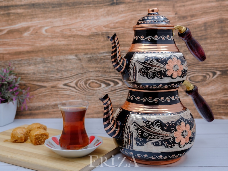 Puede incluir: Un juego de t&eacute; turco tradicional con acabado negro y cobre. La tetera tiene intrincados dise&ntilde;os florales y un mango de madera. El juego incluye un vaso de t&eacute; y un plato de baklava.