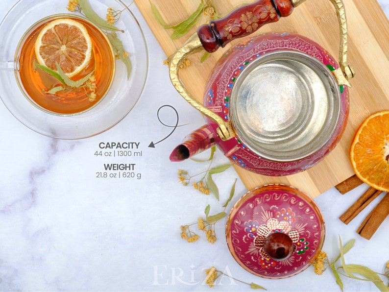 May include: A pink metal teapot with a gold handle and lid. The teapot has a floral design painted on it. The teapot is sitting on a wooden cutting board. The teapot has a capacity of 44 oz | 1300 ml and weighs 21.8 oz | 620 g.