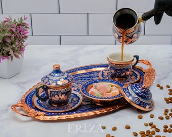 May include: A copper serving tray with blue and gold enamel designs. The tray holds a set of Turkish coffee cups, a sugar bowl, and a coffee pot. The coffee pot is pouring coffee into one of the cups. The tray is surrounded by coffee beans.