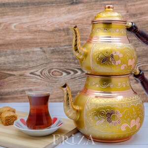 Puede incluir: Un juego de t&eacute; turco de oro y cobre con intrincados dise&ntilde;os florales. El juego incluye una tetera con dos compartimentos y un vaso peque&ntilde;o para servir el t&eacute;.
