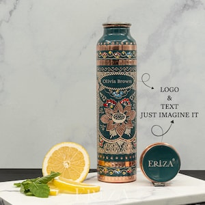 May include: A teal and copper-colored water bottle with floral and geometric patterns. The bottle has a copper lid and base. The text "Olivia Brown" is on the bottle. A matching teal coaster with the brand name "ERIZA" is also present.