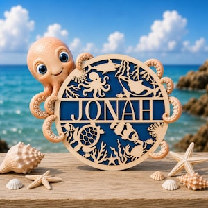 Peut inclure: Une figurine de pieuvre de couleur claire tenant un panneau circulaire en bois avec le nom JONAH découpé au centre. Le panneau présente des silhouettes découpées au laser d'un requin, d'une tortue, d'un poisson-clown et de coraux sur fond bleu.