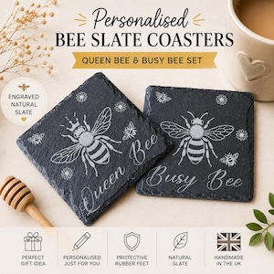 May include: Two square black slate coasters featuring engraved bee designs. One coaster displays a bee with a crown and the text Queen Bee, while the other shows a bee and the text Busy Bee. Both include small flower accents and rough edges.