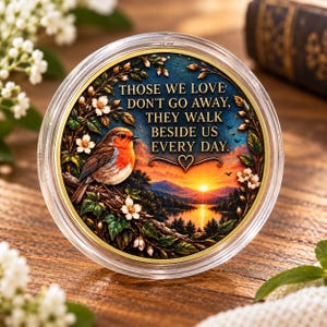 Peut inclure: Une plaque décorative circulaire représentant un rouge-gorge perché sur une branche avec des fleurs blanches. L'arrière-plan montre un coucher de soleil sur un lac et des montagnes. Le texte indique : THOSE WE LOVE DON'T GO AWAY, THEY WALK BESIDE US EVERY DAY.