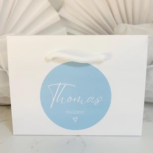 May include: White gift bag with a blue circle and the text "Thomas Pageboy" in white script. A small white heart is below the text.