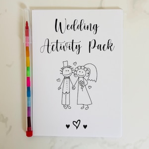 May include: A white card with the text "Wedding Activity Pack" in black lettering. A black and white illustration of a bride and groom holding hands is below the text. Three black hearts are at the bottom of the card.