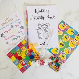 May include: A wedding activity pack with a variety of games and activities, including a "I Spy Super Star" game, a wedding-themed bingo card, a coloring page of a bride and groom, a set of smiley face stickers, and a bubble wand.