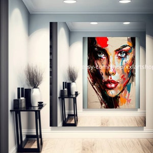 May include: Abstract painting of a woman's face with colorful brushstrokes and a textured background. The painting is framed and hanging on a wall in a modern interior.