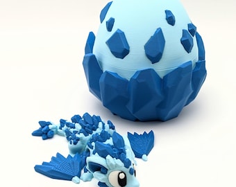 May include: A light blue dragon figurine with dark blue crystal-like detailing, next to a matching egg-shaped container. The egg is light blue with dark blue crystal shapes. The dragon has large eyes and detailed wings.