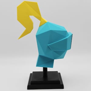 May include: A low-poly style sculpture of a knight helmet in bright cyan with a yellow plume on top. The helmet is mounted on a black vertical post attached to a square black base, creating a geometric display piece for a desk or shelf.