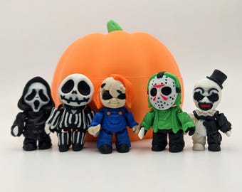 Puede incluir: Una colección de cinco figuras en miniatura con temática de Halloween, que incluyen un fantasma, un esqueleto, Chucky, Jason Voorhees y un payaso, de pie frente a una calabaza naranja. Las figuras son de colores brillantes y detalladas.