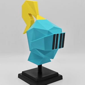 May include: A low-poly style knight helmet sculpture in bright cyan with a yellow plume on top. The helmet features a black visor with vertical slats and is mounted on a black square base with a central support rod, creating a geometric display piece.