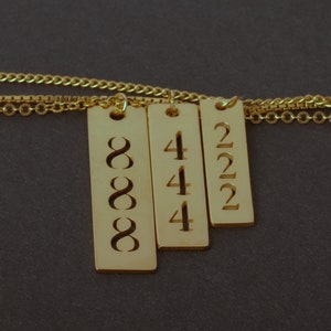May include: Gold necklace with three rectangular pendants, each with a different number engraved on it. The numbers are 888, 444, and 222.