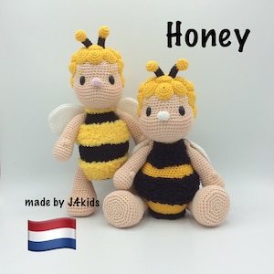Op de afbeelding: Twee gehaakte bijen knuffels, een geel en zwart met witte vleugels, de andere geel en zwart met witte vleugels en een geel hoofd. De knuffels zitten op een wit oppervlak. De tekst "Honey" is in zwart boven de knuffels geschreven. De tekst "made by J4kids" is onder de knuffels geschreven. Een Nederlandse vlag is onder de tekst.