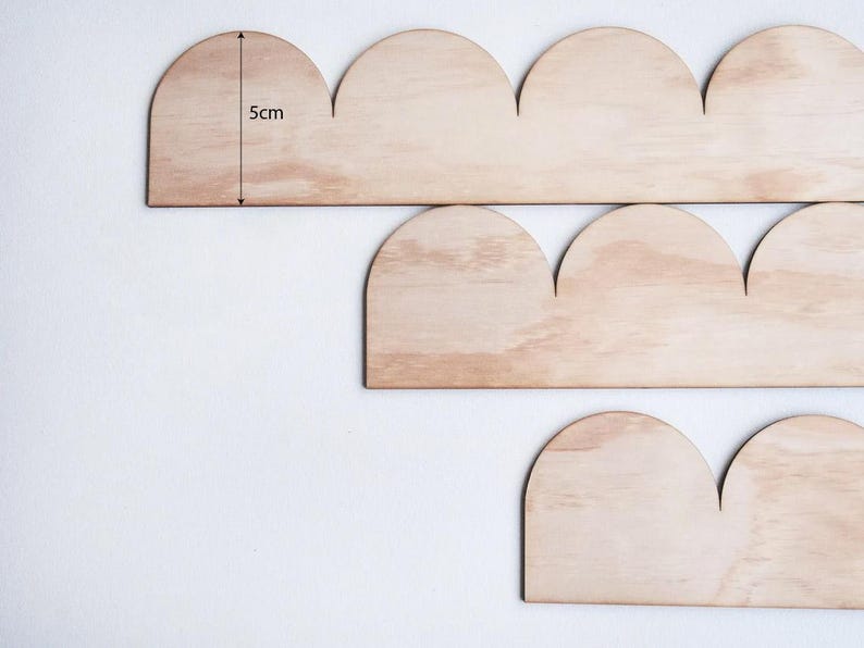 May include: Wooden cloud-shaped decorative pieces. The pieces are made of light-colored wood and are approximately 2 inches tall. The image shows several pieces arranged in a staggered pattern against a white background. The pieces are likely for home decor.