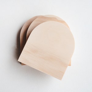 May include: Three unfinished wooden arches stacked on top of each other. The arches are made of light-coloured wood and have a smooth, rounded surface.