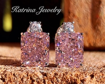 May include: A pair of pink rectangular stud earrings with a sparkling, faceted design. Each earring has a smaller, round, clear stone on top. The earrings are set on a textured, brown surface. The text "Katrina Jewelry" is visible.