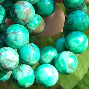May include: A strand of green turquoise beads with brown marbling. The beads are round and smooth, and they are strung together on a clear string.