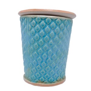 Può includere: Un vaso di ceramica blu turchese con un motivo a rombi in rilievo. Il vaso ha un coperchio ed è realizzato in uno stile semplice e moderno.