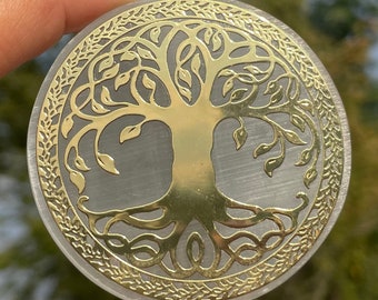 May include: A white selenite crystal with a gold-toned tree of life design etched into the surface. The tree of life design features intricate branches and roots.