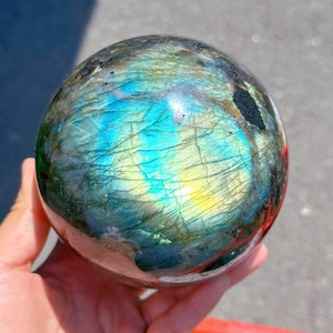 May include: A polished labradorite sphere with iridescent blue, green, and yellow colours. The sphere is smooth and has a high gloss finish.