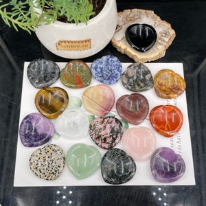 May include: A collection of 15 heart-shaped crystal stones with various colors and patterns. Each stone has a symbol etched into the surface. The stones are arranged on a white surface.