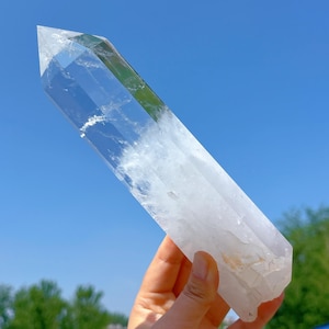 Könnte beinhalten: Eine große, klare Quarzkristallspitze mit doppelter Endung. Der Kristall ist glatt und poliert, mit einem leichten Grünstich, der im Licht sichtbar ist.