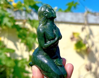 May include: A green jade sculpture of a woman kneeling with her hands clasped in front of her chest. The sculpture is highly detailed and has a smooth, polished finish.