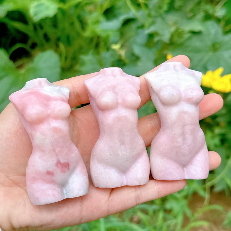 Op de afbeelding: Drie roze en witte gesneden stenen sculpturen van de menselijke torso. De sculpturen zijn glad en hebben een gepolijste afwerking.