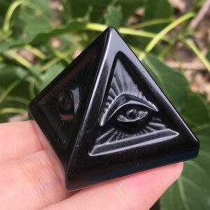May include: Black obsidian pyramid with two carved eyes, a popular crystal for protection and grounding.