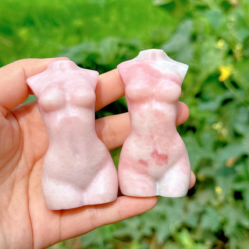 Op de afbeelding: Twee roze en witte torso sculpturen gemaakt van gepolijst steen. De sculpturen zijn glad en hebben een natuurlijke, organische uitstraling.
