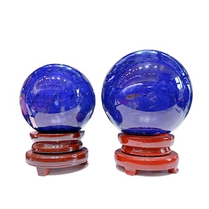 Op de afbeelding: Twee blauwe kristallen bollen op houten standaards. De grotere bol heeft een diameter van ongeveer 10 cm en de kleinere een diameter van ongeveer 7,5 cm.