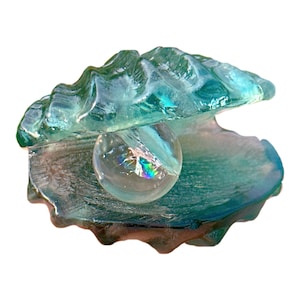 May include: A glass clam shell sculpture with an iridescent glass pearl inside. The shell is a light blue colour and has a textured surface.