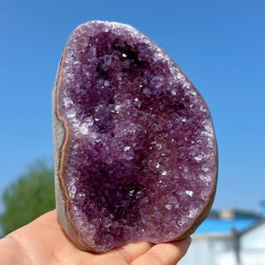 Può includere: Una grande geode di ametista con un interno di cristallo viola. La geode è di formazione naturale e ha un esterno ruvido.
