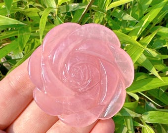 May include: A pink rose quartz crystal carved into the shape of a rose. The crystal is smooth and polished, with a delicate swirl pattern.