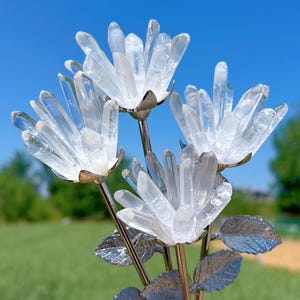 Puede incluir: Un ramo de flores de cristal de cuarzo transparente con tallos y hojas de metal plateado. Las flores están dispuestas en forma de jarrón.